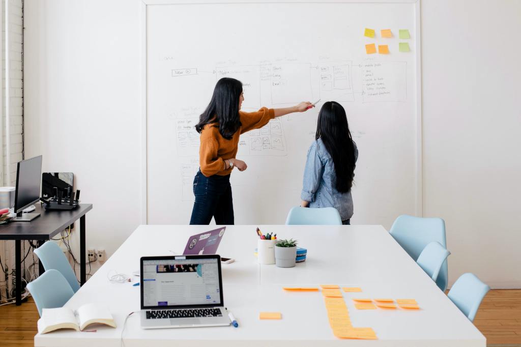photo of women discussing something in front of a whiteboard -- fancy comma blog