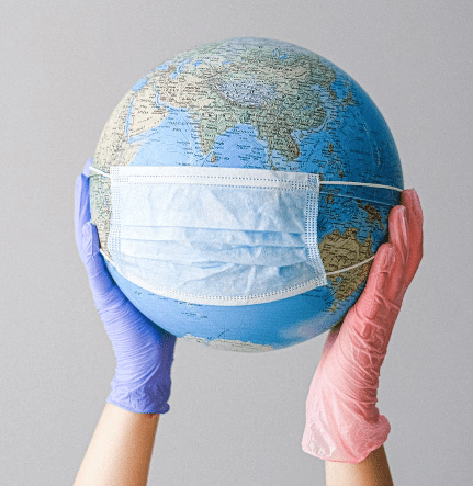 photo of gloved person holding up a globe wearing a facemask