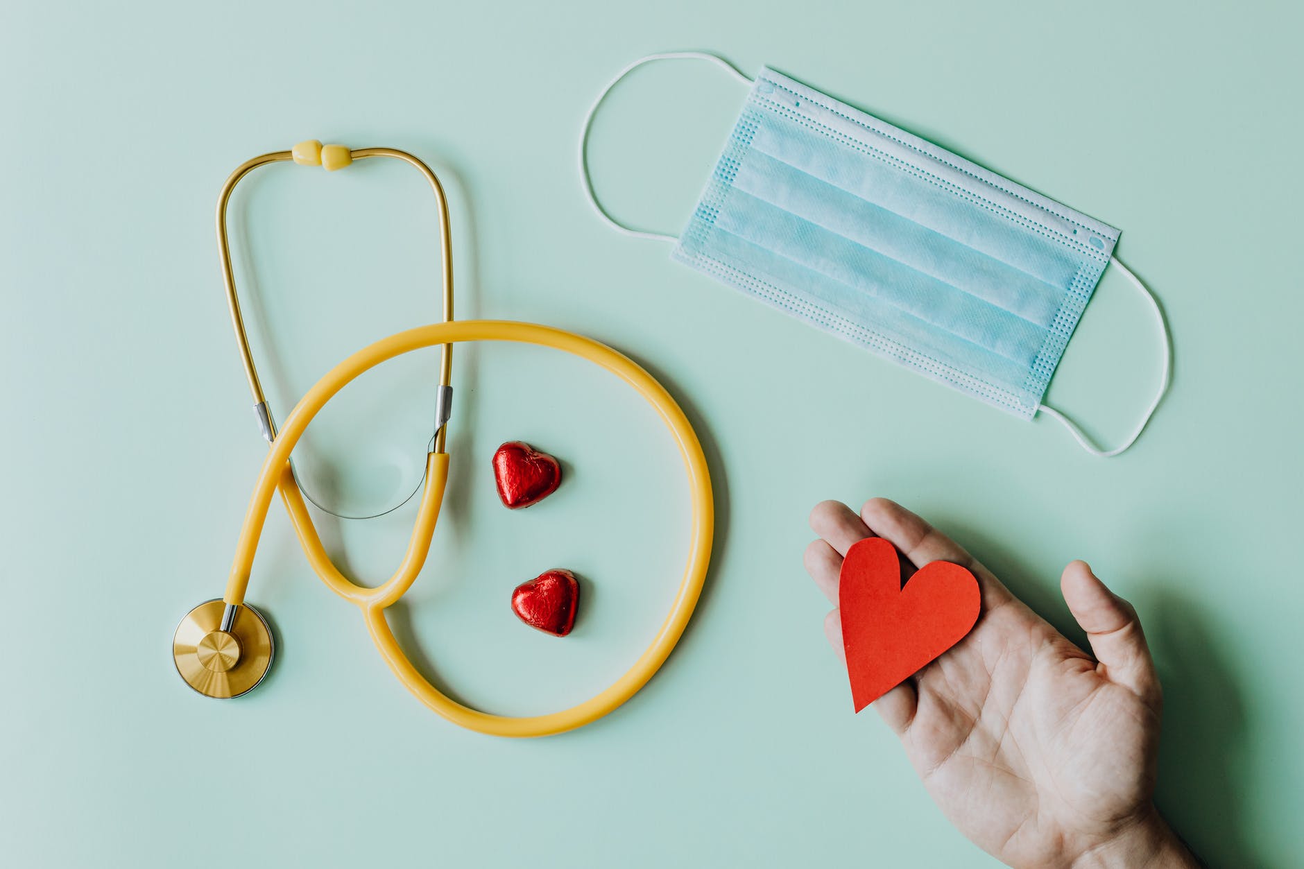 image of a stethoscope, mask, and person holding a cutout of a heart shape