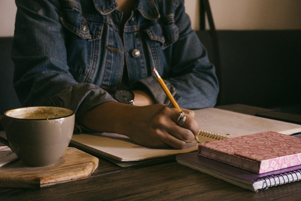 photo of woman sitting at a desk, writing with a pencil in a notebook