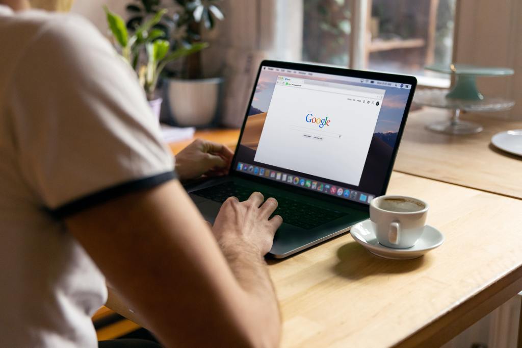 person sitting at desk and typing on a laptop that has the google website open in the browser