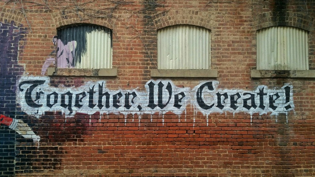 picture of the side of a brick building that has a mural that says "together, we create"